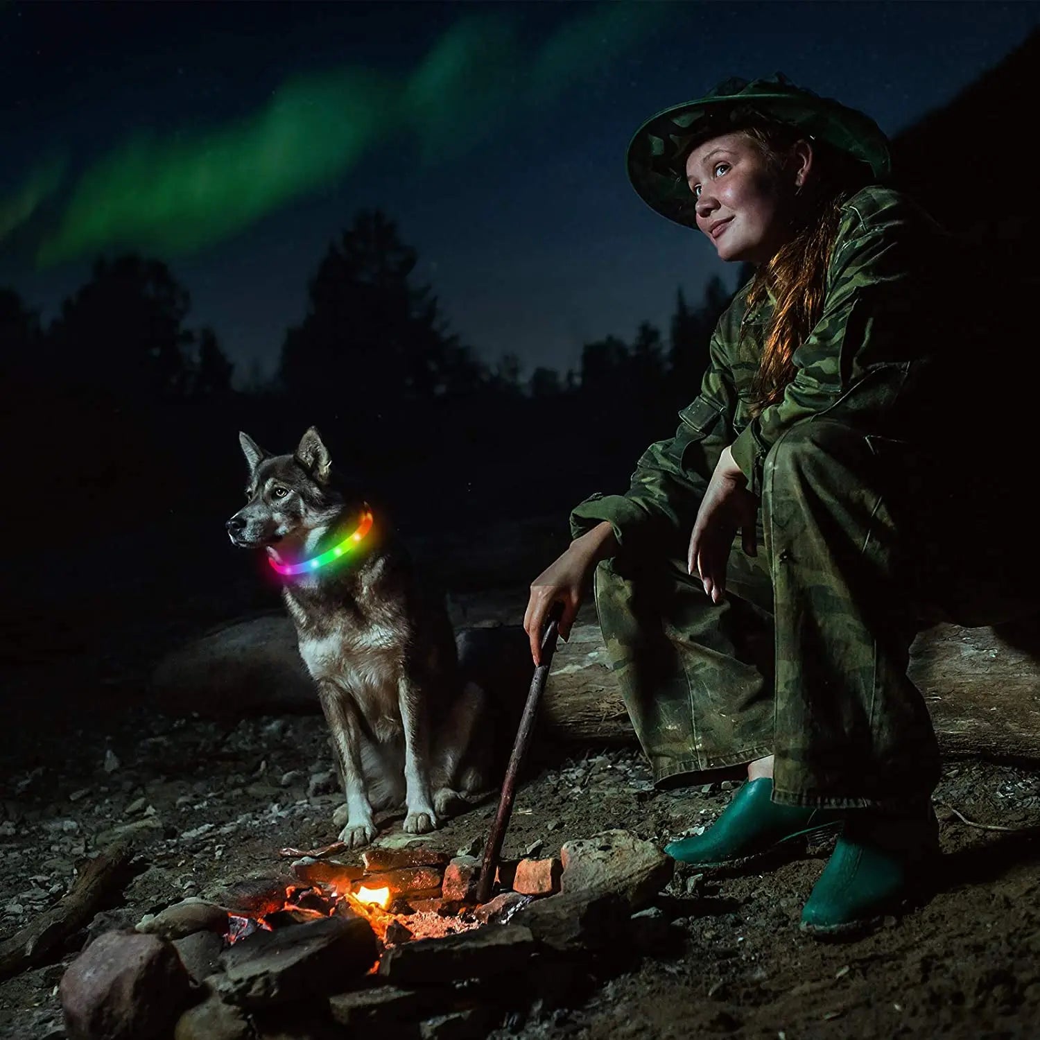 Cette dame est en train de camper en forêt avec son chien loup qui porte un collier lumineux pour chien de couleur multicolore.