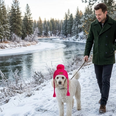 Caniche blanc portant un bonnet chien rose fuchsia en balade au bord d'une rivière.