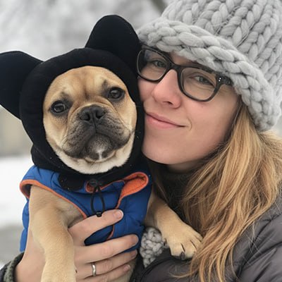 Femme tenant un Bouledogue français portant un bonnet pour chien noir à oreilles.