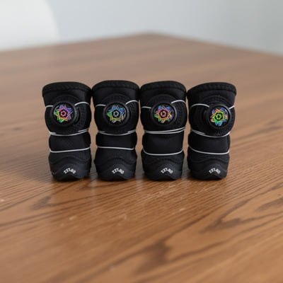 Quatre chaussures pour chien en néoprène noir alignées sur une table en bois.