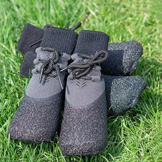 Lot de quatre chaussures pour chien grises et noires posées en gros plan sur de l'herbe verte.