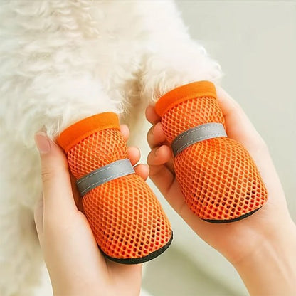 Mains tenant les pattes d'un chien blanc chaussé de chaussures pour chien orange à bandes réfléchissantes.