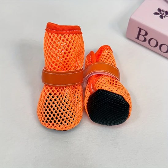 Paire de chaussures pour chien orange montrant la semelle noire antidérapante et une boîte rose.