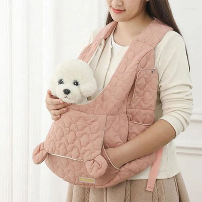 Femme tenant un petit chien blanc dans un sac de transport rose avec logo jaune en bas.