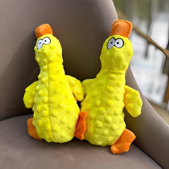 Deux exemplaires de la peluche pour chiens canard jaune posés verticalement sur un fauteuil.