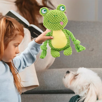 Une petite fille tend une peluche pour chiens grenouille à un petit chien blanc à poil long.