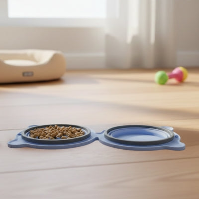 Gamelle chien bleue pliable en position plate avec croquettes, posée sur un parquet clair.