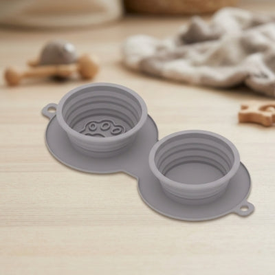Gamelles chien grises en silicone avec motif patte, posées sur une surface en bois clair.