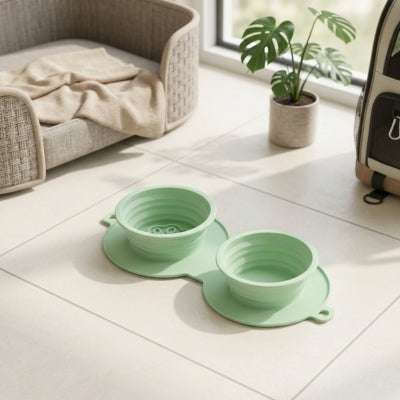 Paire de gamelles chien vertes en silicone posées sur un sol carrelé près d'un panier.