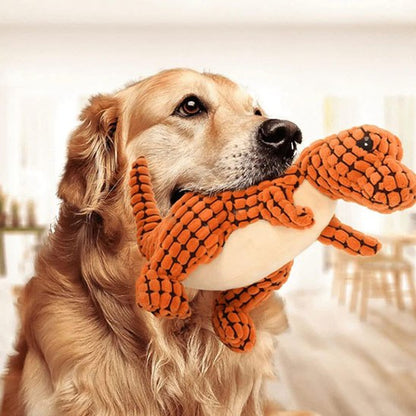 Golden Retriever de profil portant une grande peluche pour chiens dinosaure orange.