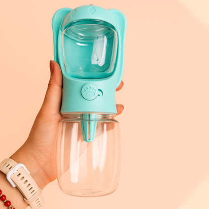 Main tenant une gourde pour chien bleue avec bouton poussoir motif patte et flacon transparent.