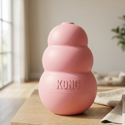 Gros plan d'un jouet Kong chien rose pastel posé sur une table en bois dans un salon.