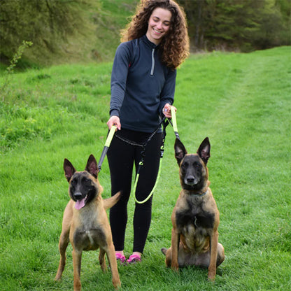 Femme en forêt tenant une laisse double pour chien avec deux Bergers Belges Malinois.