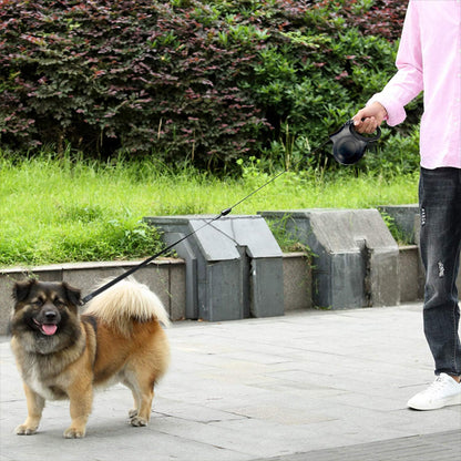 Homme en chemise rose marchant avec une laisse pour chien rétractable noire et un chien croisé.