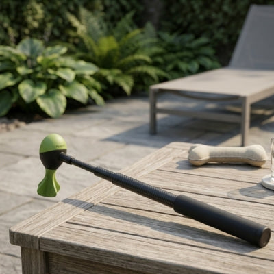 Lanceur de balle pour chien avec embout vert ailé posé sur une table de jardin en bois.