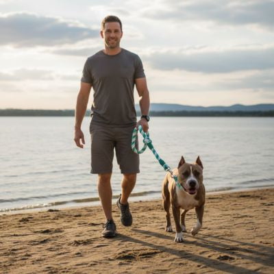 Homme marchant sur le sable avec son Pitbull attaché par une longe pour chien blanche et verte.