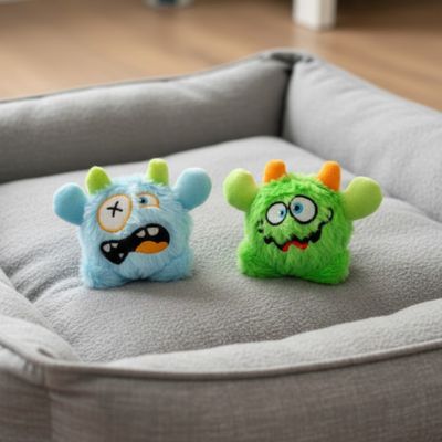 Deux modèles de jouet pour chien monstres bleu et vert posés dans un panier gris.