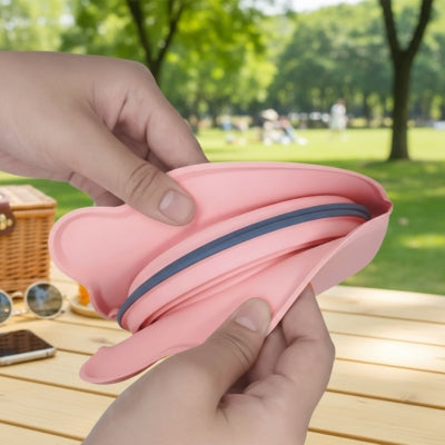 Gros plan de mains pliant une gamelle chien en silicone rose sur une table de pique-nique.