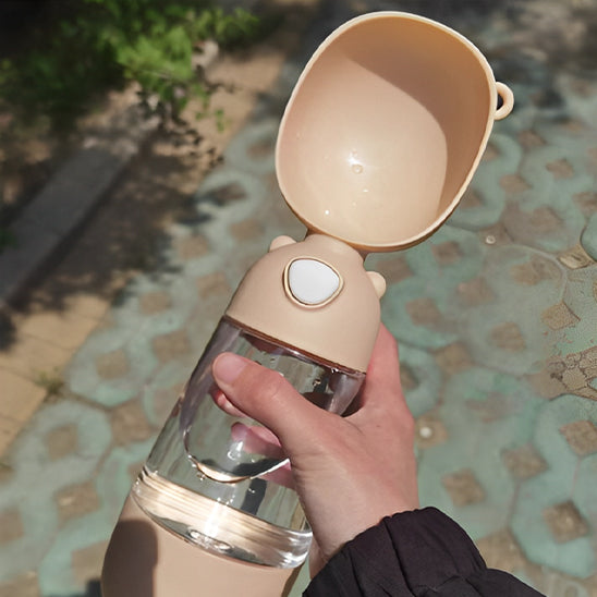 Main tenant une gourdes pour chien beige avec abreuvoir en forme de bol et bouton de verrouillage.