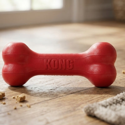 Jouet pour chien kong rouge en forme d'os posé sur un parquet avec des miettes de friandises.