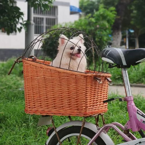 Spitz blanc dans un panier chien velo en osier avec grille sur porte-bagages d'un vélo rose.