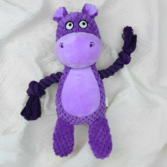Peluche pour chiens hippopotame violet avec des bras en corde sombre sur un drap blanc.