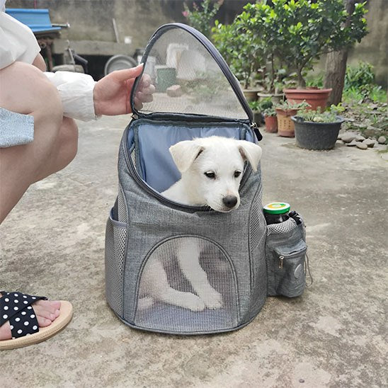 Sac a dos chien gris ouvert au sol avec un chiot blanc à l'intérieur.
