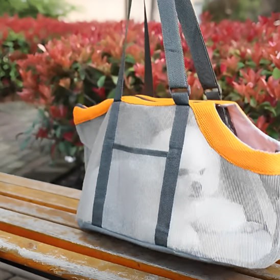 Sac de transport chien gris et orange posé sur un banc avec un chien blanc visible par transparence.