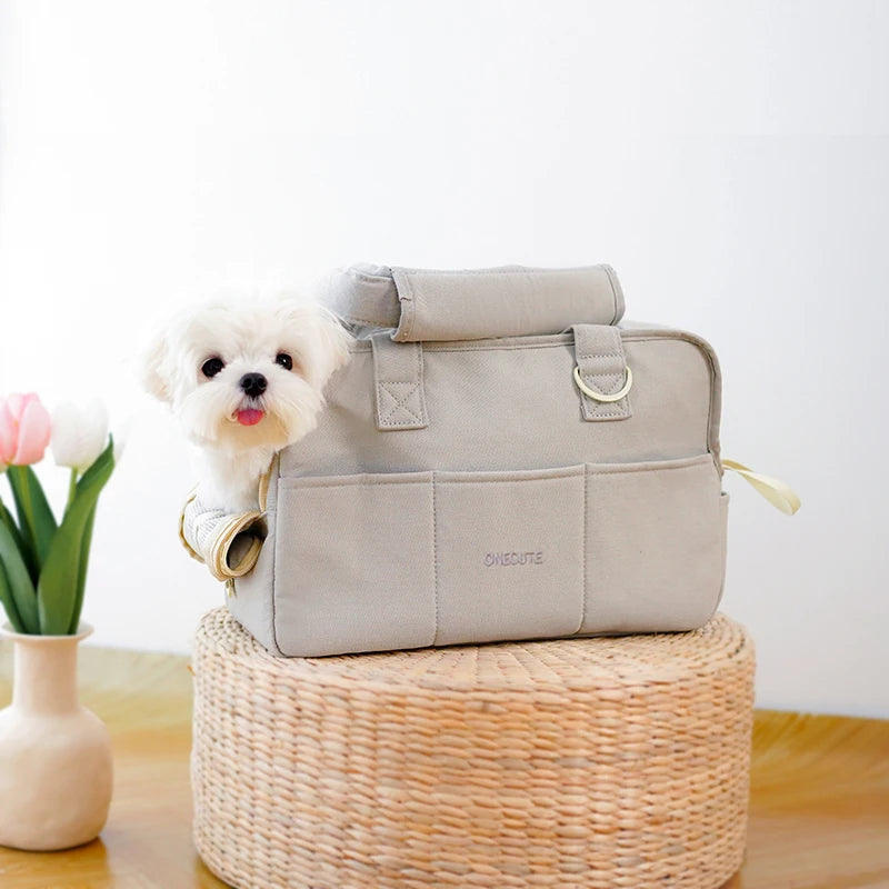 Ce caniche nain est  dans un sac de transport pour chien de couleur grise posé sur une petite table