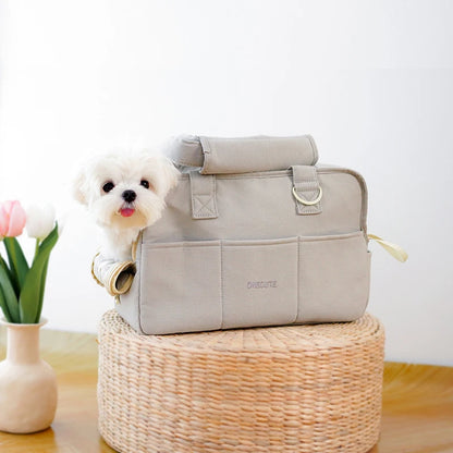 Ce caniche nain est  dans un sac de transport pour chien de couleur grise posé sur une petite table