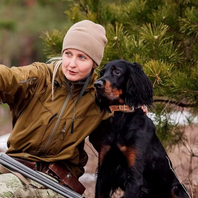 Femme en tenue de chasse avec un Setter Gordon et un sifflet à ultrason pour chien autour du cou.