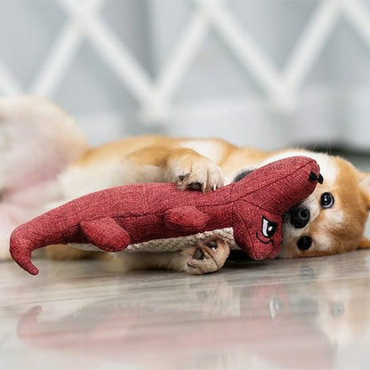 Shiba Inu allongé au sol jouant avec sa peluche pour chien crocodile de couleur rouge.