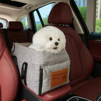 Bichon blanc installé dans un siege auto chiens gris sur l'accoudoir central d'une voiture.