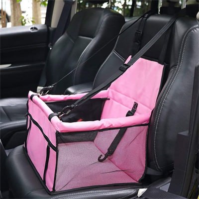 Panier vide rose type siege auto pour chien avec sangles de sécurité installé en voiture.