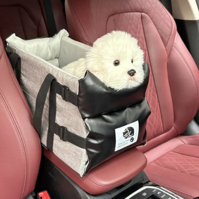 Bichon frisé dans un siege auto pour chiens gris posé sur l'accoudoir central d'une voiture.