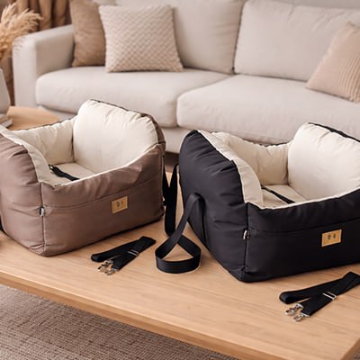 Un siege auto pour chiens beige et un noir posés sur une table basse en bois.