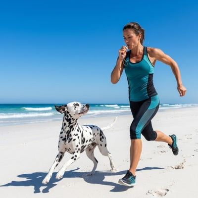 Femme courant sur la plage avec un Dalmatien et utilisant un sifflet ultrason pour chien.