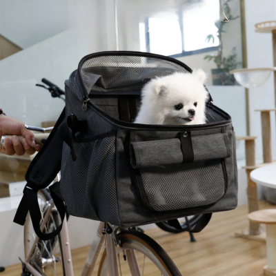 Petit Spitz blanc assis dans un panier vélo pour chien gris fixé sur le guidon d'un vélo.