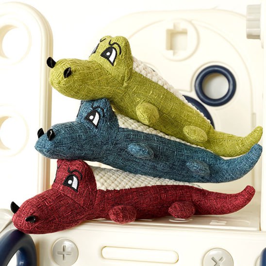 Peluche pour chien en forme de crocodile vert, bleu et rouge empilées sur un support blanc.