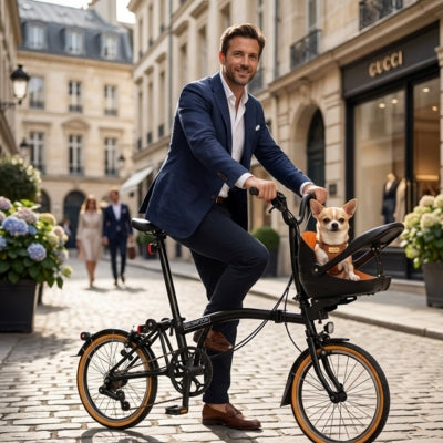 Homme en costume sur un vélo pliant avec un chihuahua dans un panier noir, rue pavée.