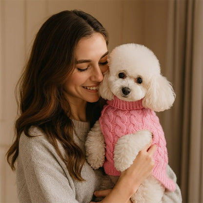 Femme tenant un Bichon Frisé avec un vetement chien, pull rose à col roulé, en intérieur.